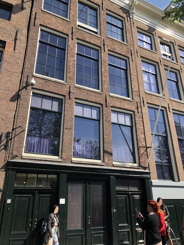 People pose in front of the Anne Frank Huis in Amsterdam. Faces of people have been masked for privacy.